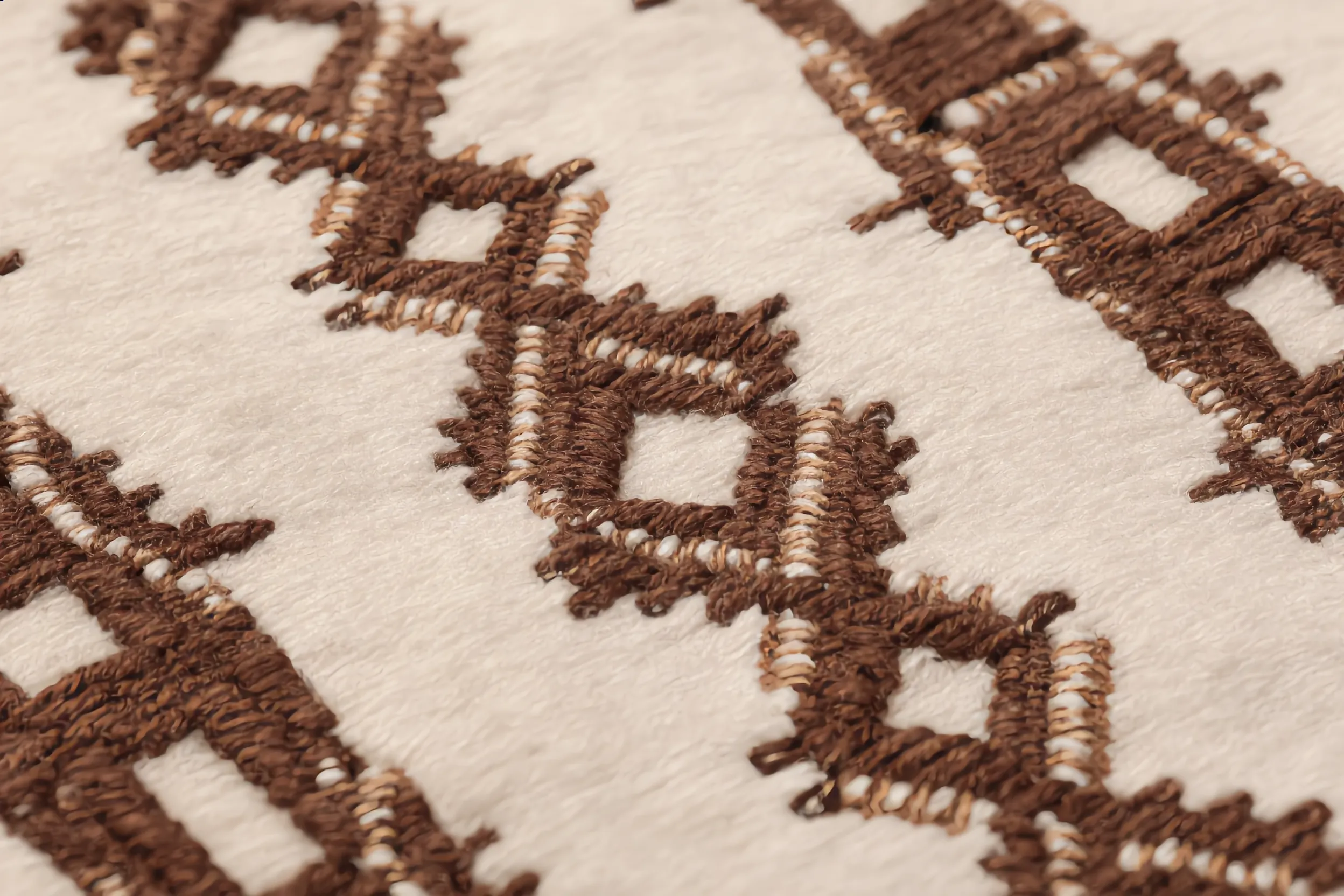 Macro close-up of a Beni Ourain rug surface showing thick ivory pile with dark brown hand-knotted diamond and lozenge geometric symbols