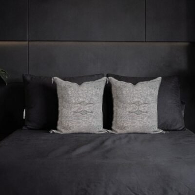 Two grey handwoven sabra silk pillow covers styled on a black upholstered bed