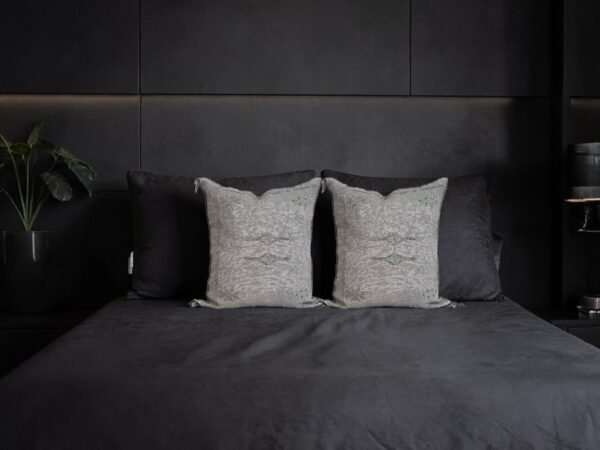 Two grey handwoven sabra silk pillow covers styled on a black upholstered bed