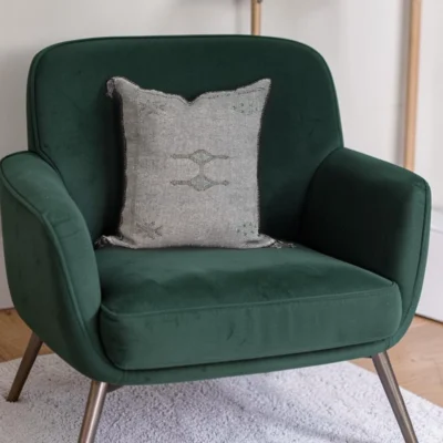 Grey Moroccan sabra silk cushion styled on an emerald green velvet armchair