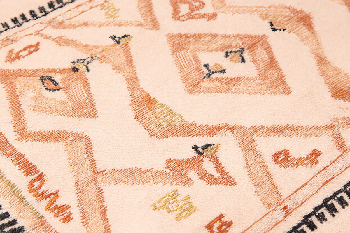 Macro close-up of Azilal rug motifs showing diamond lozenges and zigzag symbols in natural dyes on ivory wool