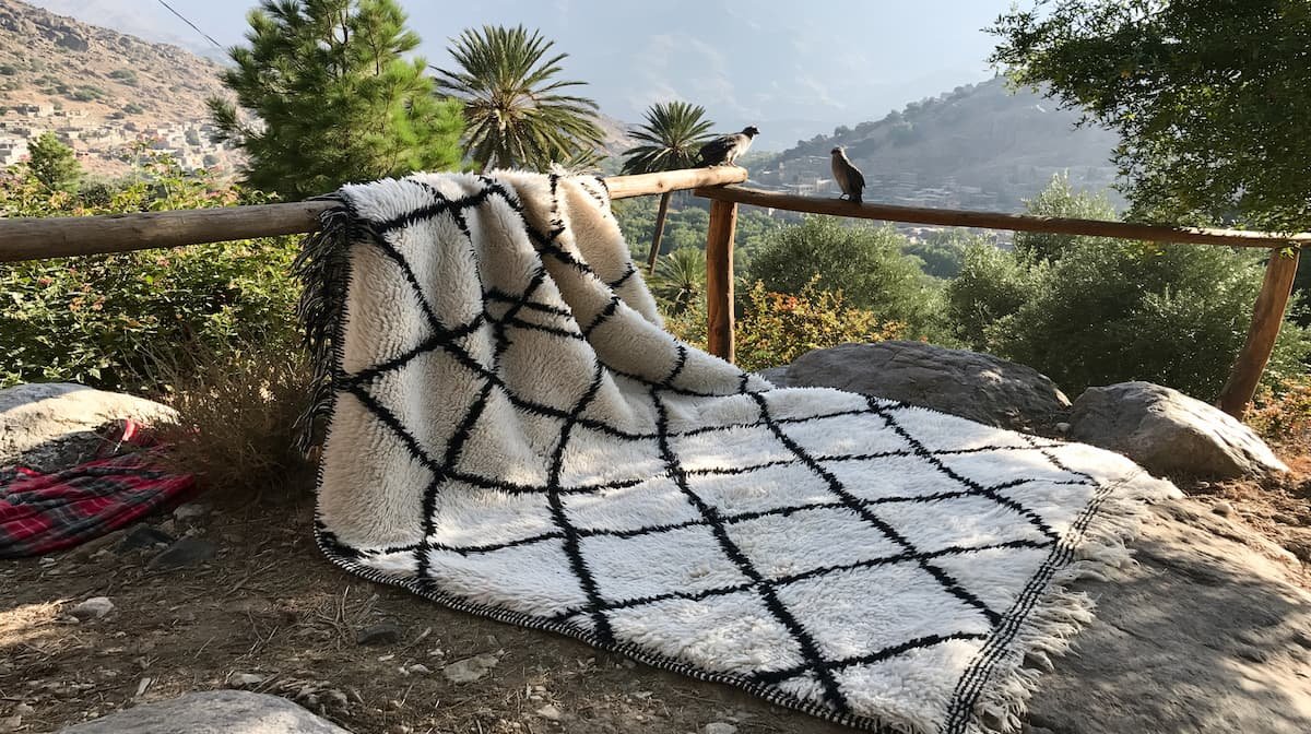 Authentic Moroccan Beni Ourain rug hanging outdoors in mountain sunlight for seasonal airing and care