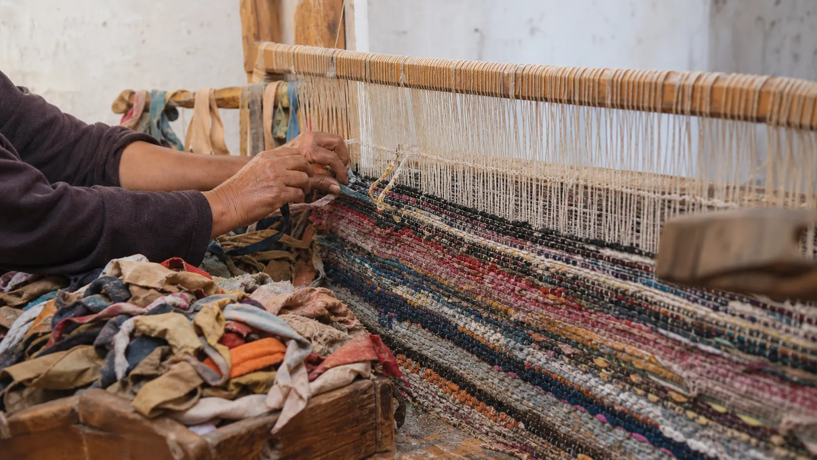 Moroccan artisan weaving reclaimed fabric strips into a Boucherouite rug on a wooden loom