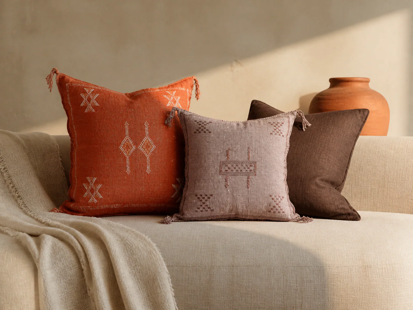 Warm Medina pillow palette with burnt-orange, dusty-mauve, and dark-brown cushions on a neutral sofa